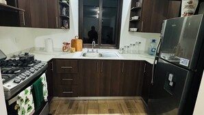 A kitchen with dark wooden cabinets, a stainless steel refrigerator, a gas stove, and a window above the sink.