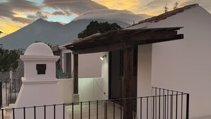 A modern building with a white facade, a balcony with a metal railing, and a view of a mountain in the background.