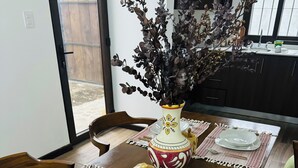 A dining table set with white plates, cutlery, and a decorative vase with dried flowers.