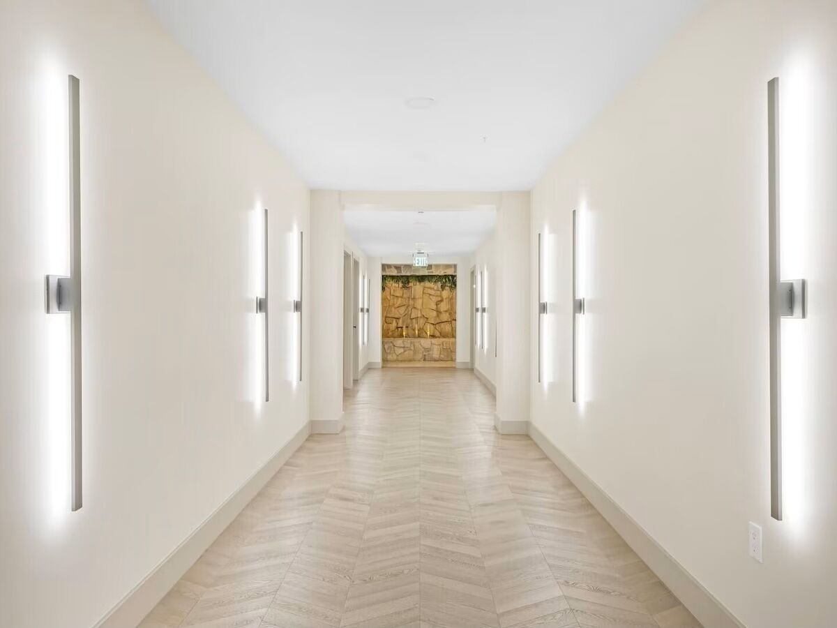 Un largo pasillo bien iluminado con suelo de espiga y una pared de piedra decorativa al final.