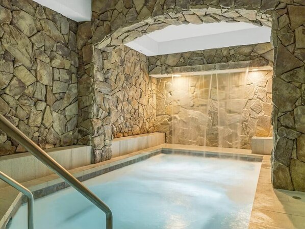 Et spaområde med stenvæg, jacuzzi og træbænk.