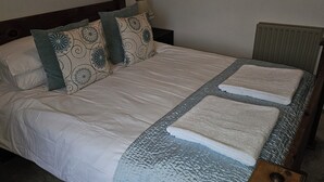 A neatly made bed with a white duvet, two pillows with a floral pattern, and two folded towels on the bed.