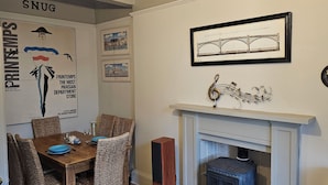 A dining area with wicker chairs, a wooden table, and a fireplace.