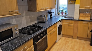 A modern kitchen with wooden cabinets, a gas stove, a built-in oven, a washing machine, and a sink.