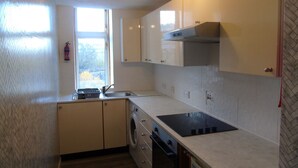 A kitchen with white cabinets, a built-in oven, a dishwasher, and a window with a view of trees. - Snug - Grian-aig Apartment (Greenock)