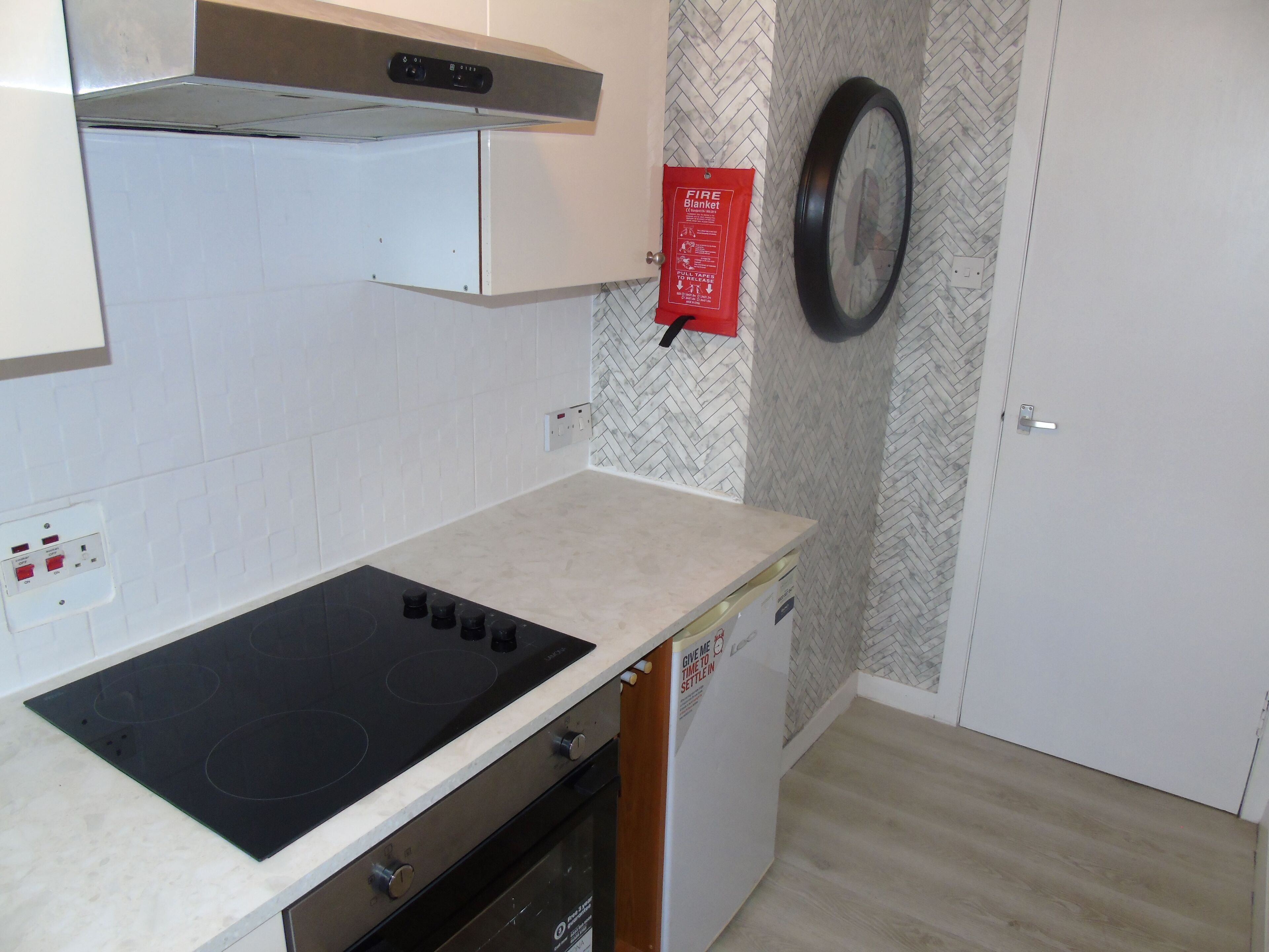 Een keuken met een zwart inductiekookplaatje, witte kasten, een backsplash met een herringbone-patroon en een branddeken aan de muur.