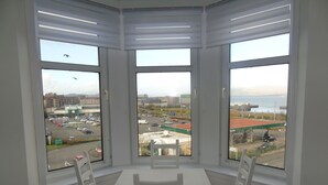 A corner room with a bay window overlooking a parking lot and a gas station. - Snug - Grian-aig Apartment (Greenock)