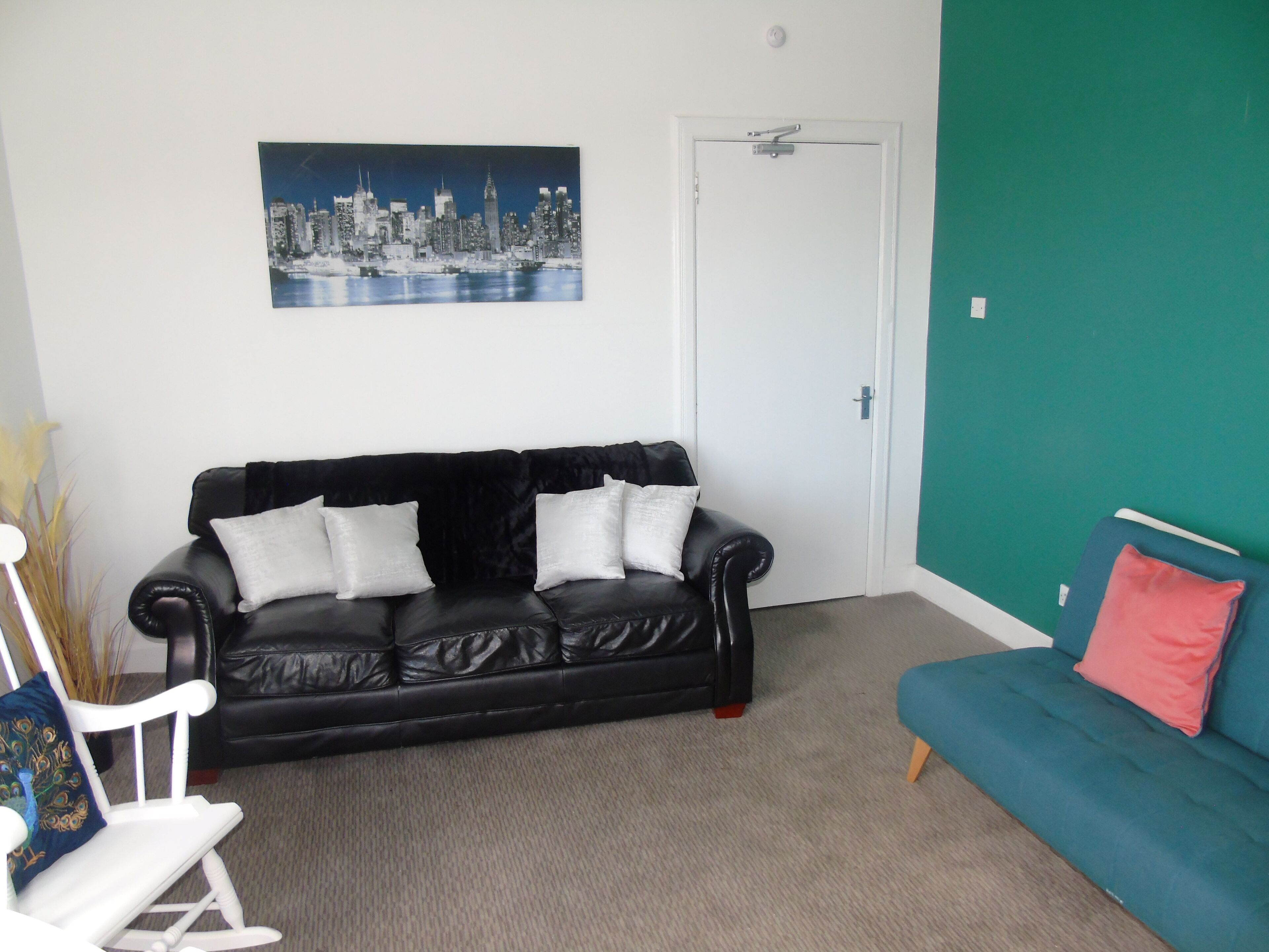 Un salon avec un canapé en cuir noir, un canapé de couleur turquoise et un fauteuil à bascule blanc.
