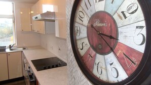 A kitchen with a large clock on the wall, a window, and cabinets. - Snug - Grian-aig Apartment (Greenock)