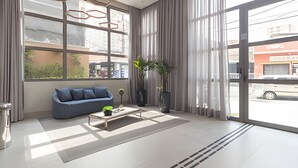 A modern living room with a blue sofa, a coffee table, and large windows with curtains. - Prime Smart Santa Cruz (São Paulo)
