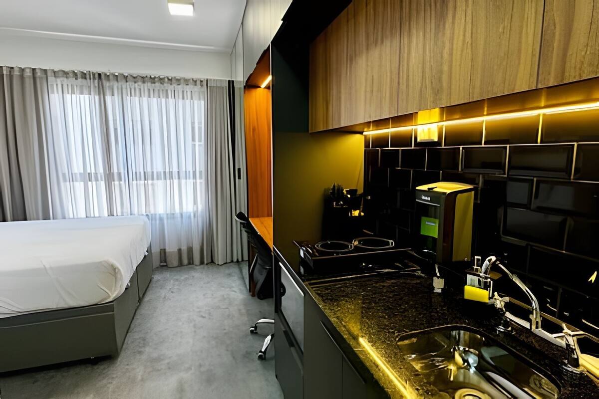 A compact hotel room with a bed, a kitchenette, and a window with curtains.