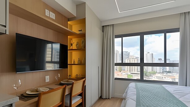A hotel room with a bed, a desk with chairs, a flat-screen TV, and a large window with a city view. - Prime Smart Santa Cruz (São Paulo)