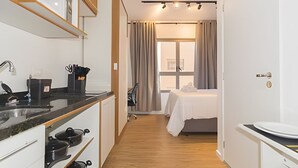 A modern hotel room with a kitchenette, a bed with a white duvet, and a window with curtains. - Prime Smart Santa Cruz (São Paulo)
