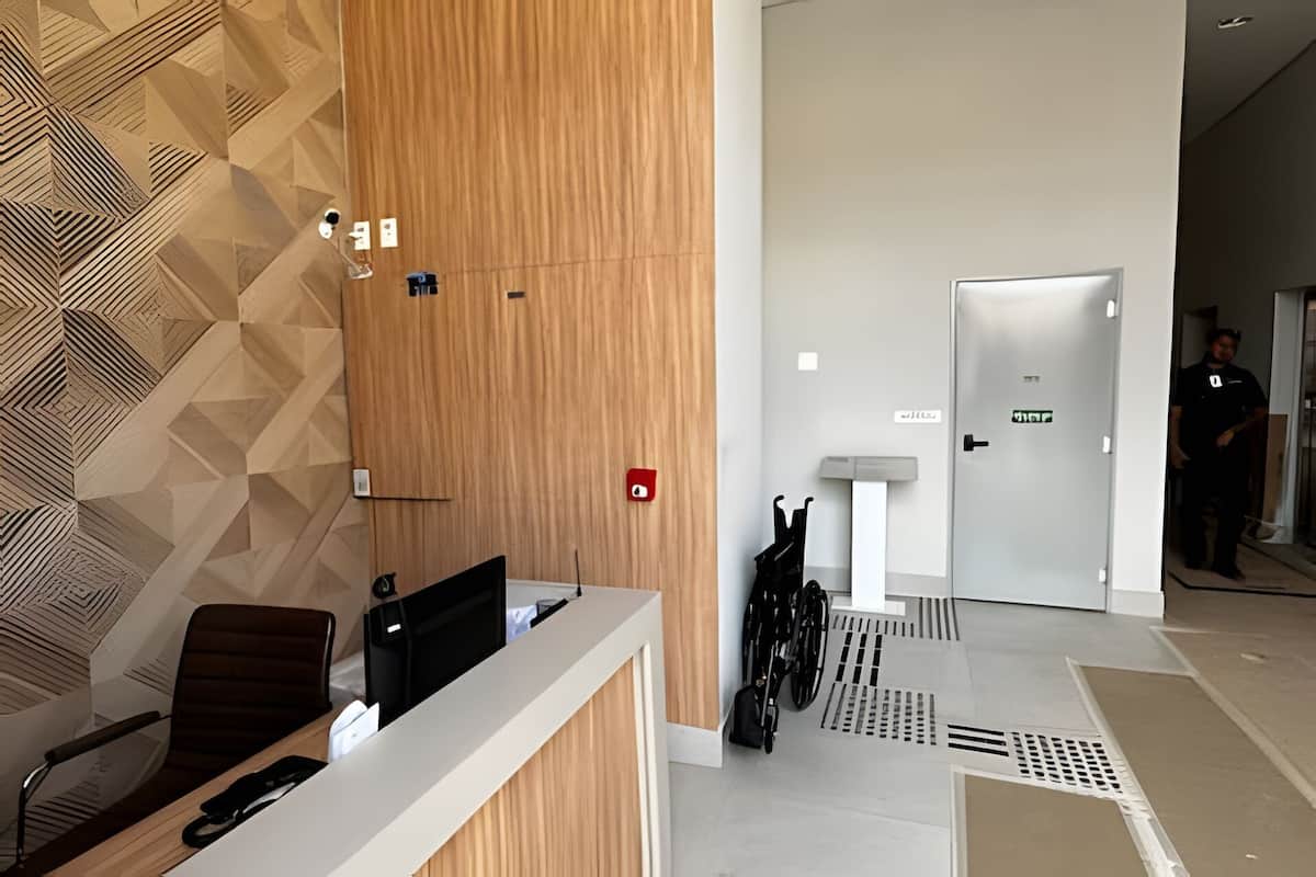 A modern reception area with a wooden panel wall, a reception desk, and a white counter. There are bicycles parked near a door with an emergency exit sign.