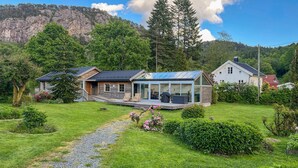 A modern house with a glass extension, surrounded by lush greenery and a mountainous backdrop. - Lovely home in Flekkefjord with sauna (Flekkefjord)