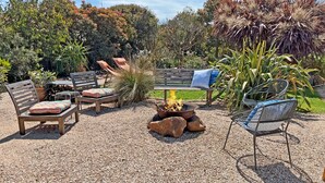 An outdoor seating area with wooden furniture, a fire pit, and a variety of plants. - Infinity at Surf Beach (Surf Beach)