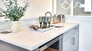 A modern kitchen with a white countertop, a potted plant, and a tray with glassware. - Modern Bachelorette Retreat — Rooftop, Karaoke, Near Downtown Broadway. (Nashville)