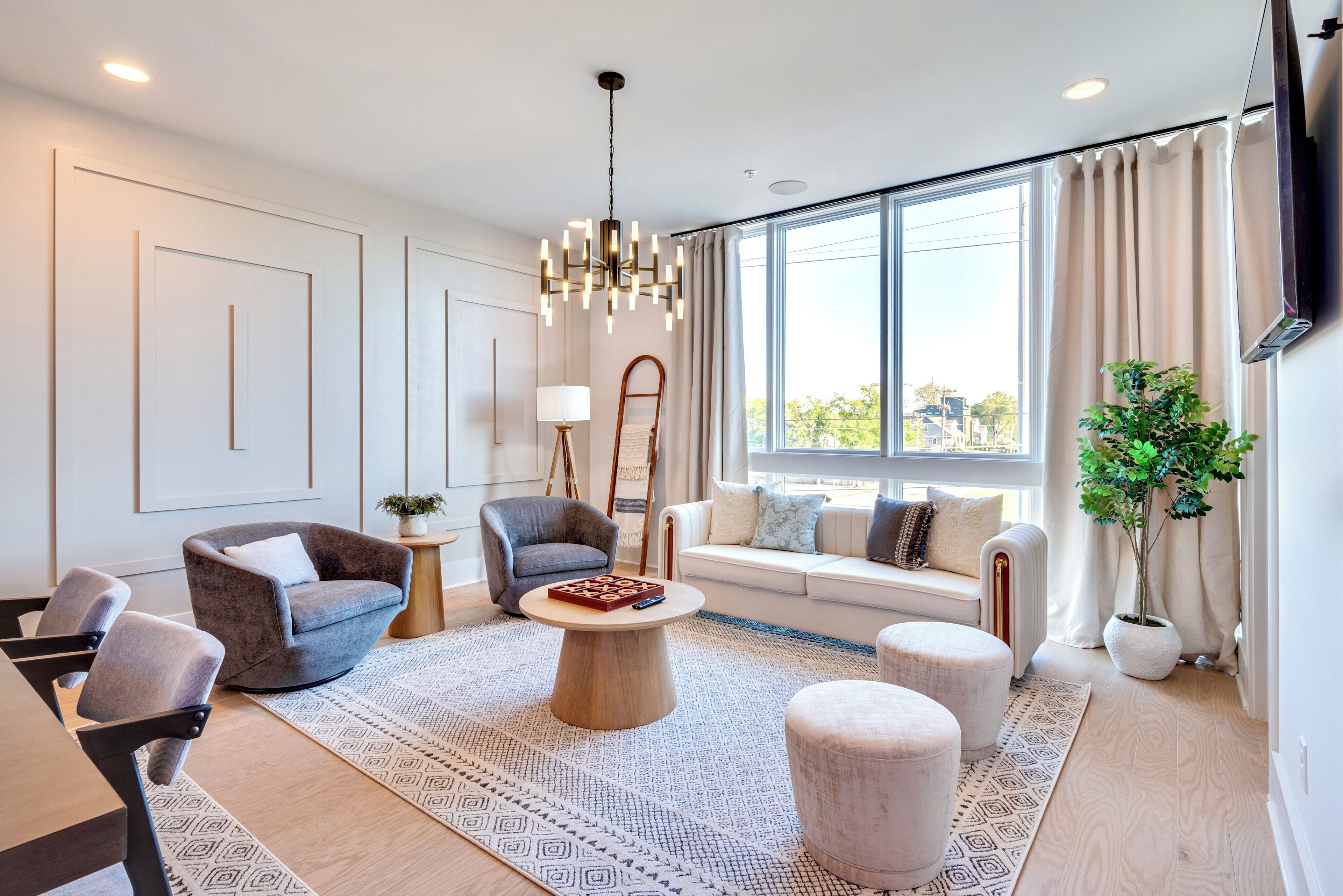 A modern living room with a sofa, armchairs, a coffee table, and a large window with curtains.
