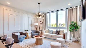 A modern living room with a sofa, armchairs, a coffee table, and a large window with curtains. - Modern Bachelorette Retreat — Rooftop, Karaoke, Near Downtown Broadway. (Nashville)