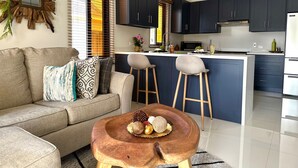 Una sala de estar moderna con sofá, una mesa de centro y una cocina con armarios oscuros y una isla central.