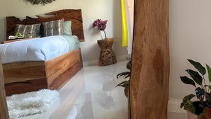 Un dormitorio con una cama de madera, un felpudo blanco y mullido, una planta en maceta y un espejo grande.