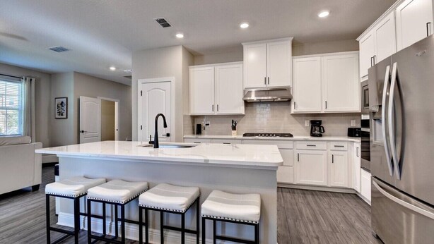 A modern kitchen with white cabinetry, a large island with stools, stainless steel appliances, and recessed ceiling lighting.