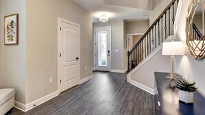 A spacious hallway with a wooden floor, a staircase with a black railing, and a white door.