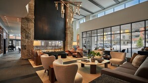 A modern lounge area with a stone column, comfortable seating, a fireplace, and large windows offering city views. - Luxury Mountain Resort (Park City)