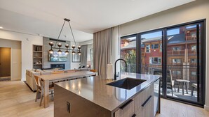 A modern kitchen with a large island, a dining area, and a view of a building through large windows. - Luxury Mountain Resort (Park City)