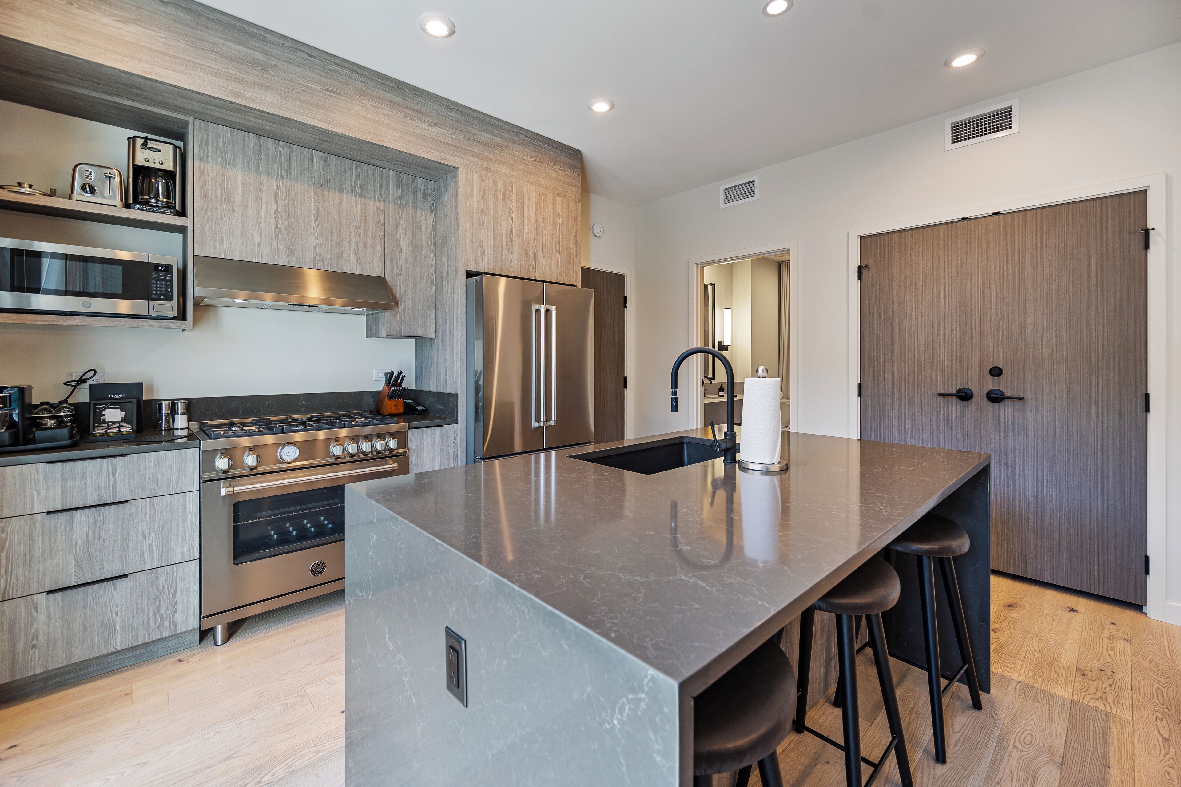 A modern kitchen with a central island, stainless steel appliances, and wooden cabinetry.