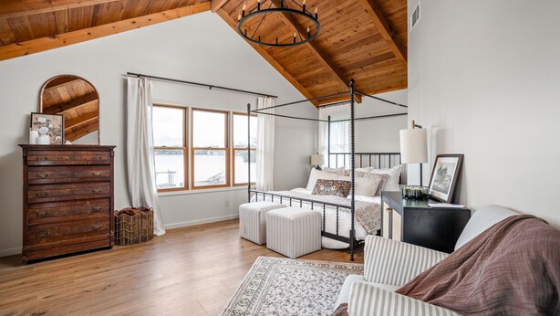 Une chambre à coucher avec un lit à baldaquin, une commode en bois, une grande fenêtre et un lustre.