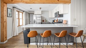 Une cuisine moderne dotée d’un grand îlot central, de poutres en bois, d’armoires blanches et d’une poubelle.