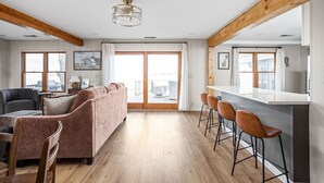 Un vaste espace de vie comprenant un grand canapé, une table à manger avec des tabourets de bar et un coin cuisine doté d’un plan de travail blanc.