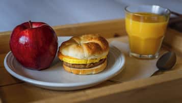 Una bandeja de desayuno con una manzana roja, un sándwich y un vaso de jugo de naranja.