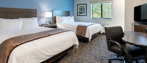 A hotel room with two beds, a desk, a chair, a television, and a window with a view of trees.