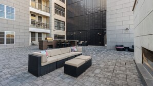 Un espacio al aire libre con sala de estar, que incluye un sofá, un reposapiés, una parrilla y una mesa de comedor.