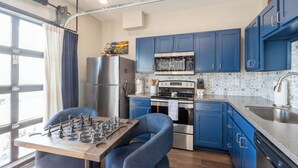 Una cocina moderna con armarios azules, electrodomésticos de acero inoxidable y un tablero de ajedrez sobre la mesa.