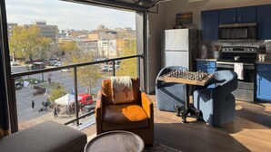 Una habitación moderna con un ventanal grande, una mesa de ajedrez, un sofá y una zona de cocina.
