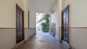 A narrow hallway with stone flooring and wooden doors, leading to a courtyard with a green plant and a building in the background. - Milano Apartments Alzaia 54 (Milan)