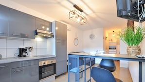 A modern kitchen with grey cabinets, a built-in oven, a coffee machine, and a dining area with a table and two chairs.