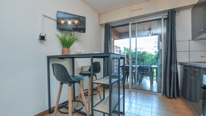 A small kitchenette with a TV, a dining area with two chairs, a potted plant, and a sliding glass door leading to an outdoor area.