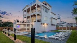 Uma casa com vários andares, piscina, área de estar externa e um elemento decorativo com água.