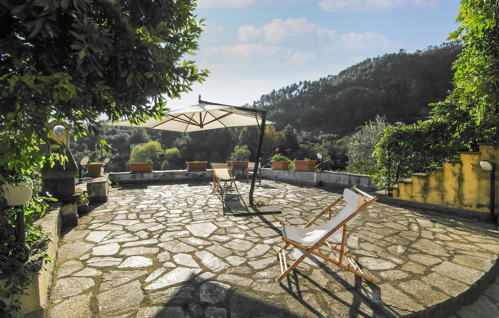 Eine Steinterrasse mit Gartenmöbeln, einer Pergola und Kübelpflanzen.
