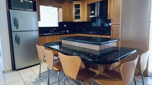 A kitchen with wooden cabinets, a stainless steel refrigerator, a black countertop island with chairs, and a microwave. - Villa Serena 2

 (San Carlos)