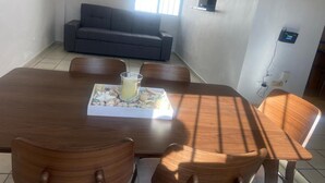 A dining area with a wooden table and chairs, a tray with food and a drink, and a sofa in the background. - Villa Serena 2

 (San Carlos)