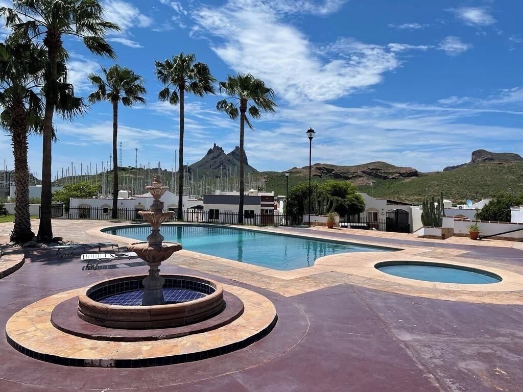 A swimming pool with a fountain, surrounded by palm trees and a mountainous backdrop.