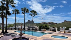 A swimming pool with a fountain, surrounded by palm trees and a mountainous backdrop. - Villa Serena 2

 (San Carlos)
