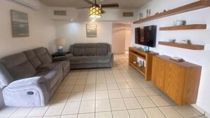 A living room with a grey sofa, a TV on a wooden stand, and a ceiling fan. - Villa Serena 2

 (San Carlos)
