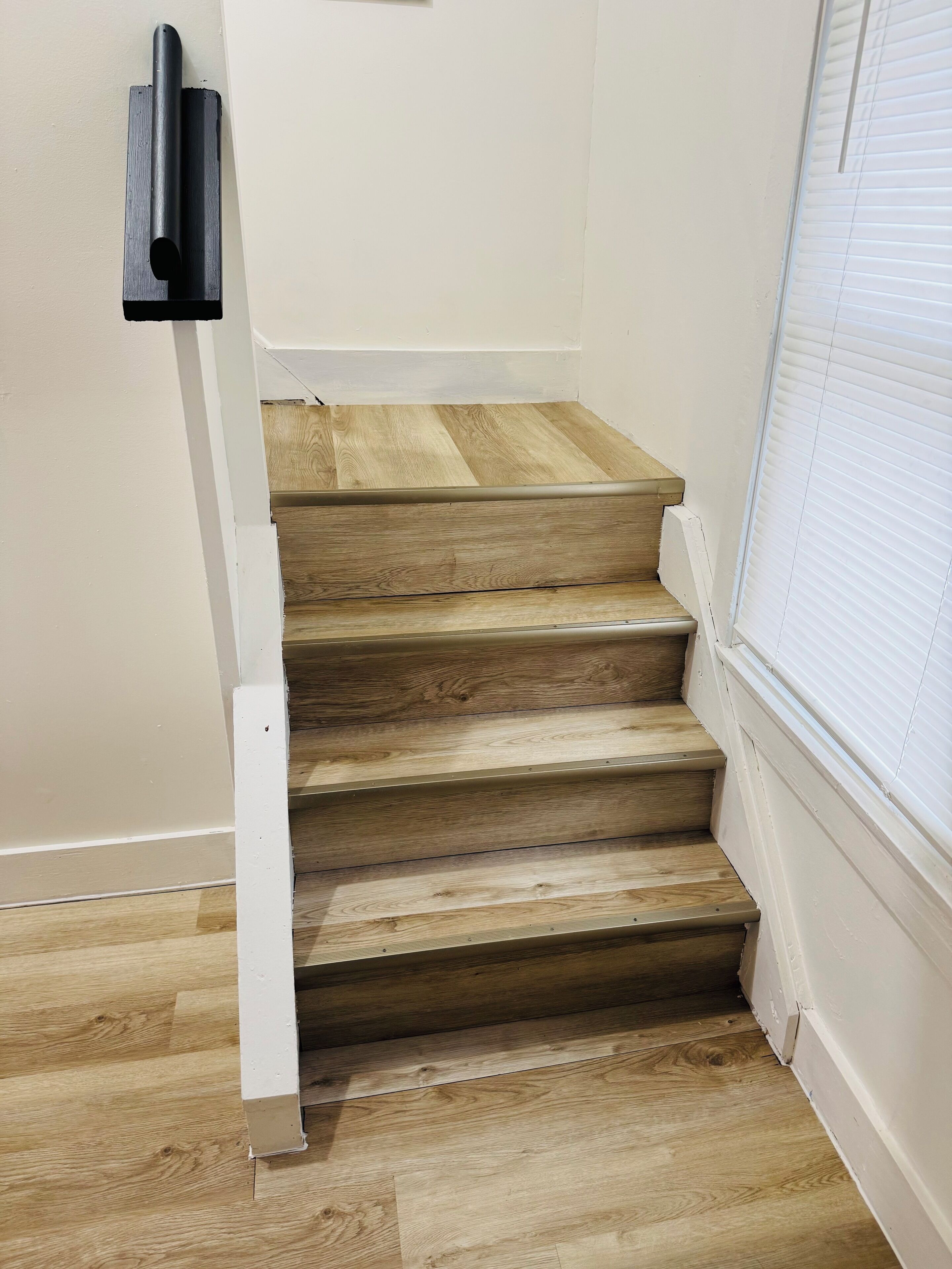 Una escalera de madera con paredes blancas y una ventana con persianas.
