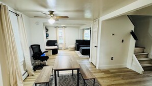 A spacious living area with a wooden floor, a ceiling fan, a dining table with benches, and a staircase leading to an upper level. - Super Modern 2-Bedroom Riverside Home @ RIT (Rochester)
